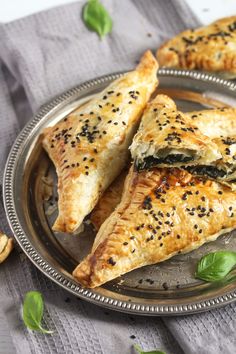 three pastries on a silver plate with green leaves and seasoning sprinkles