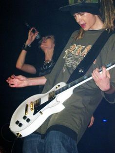 a young man holding a white guitar in his right hand and wearing a black hat