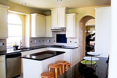 a kitchen with white cabinets and black counter tops, two stools in front of the sink