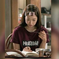 a young woman sitting at a table with a book and pen in her hand while writing