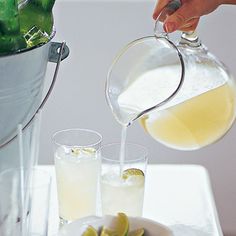 a person pours some liquid from a pitcher into two glasses on a tray with limes