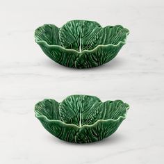 two green leaf shaped dishes sitting on top of a marble countertop next to each other