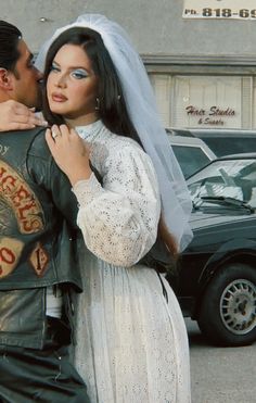 a man and woman dressed in wedding attire standing next to each other on the street