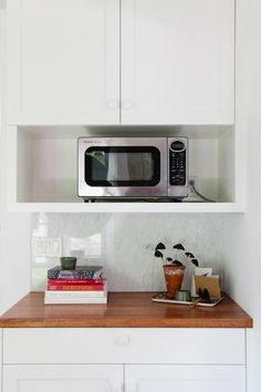 a microwave oven sitting on top of a kitchen counter next to books and coffee cups