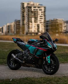 a motorcycle parked on the side of a road in front of tall buildings and grass