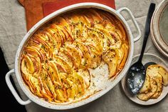 an oval casserole dish with potatoes and herbs on the side next to a spoon