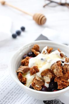 a white bowl filled with cereal and blueberries on top of a table next to an open book