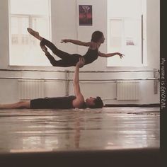 two people doing acrobatic tricks on the floor in an empty room with windows