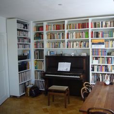 a room filled with lots of books next to a wooden table and piano in front of a bookcase