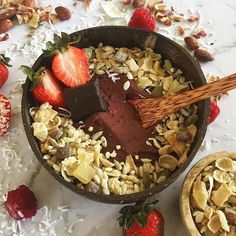 a bowl filled with granola, chocolate and strawberries on top of a table