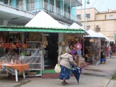 a woman walking past a market with lots of umbrellas and other items on display