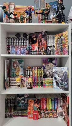 a white book shelf filled with books and anime figurines on top of it