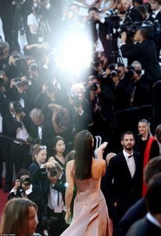 a woman in a pink dress is taking pictures on the red carpet at an event