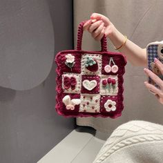 a woman holding a crocheted purse with flowers and hearts on it, in front of a mirror