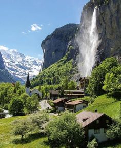 a waterfall is coming out of the side of a mountain with houses and trees around it