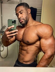 a shirtless man taking a selfie with his cell phone in the shower room