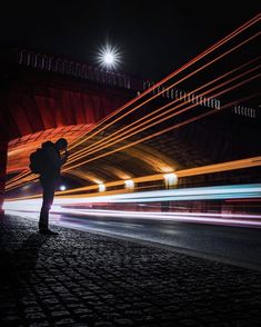 a man standing on the side of a road next to a red bridge at night