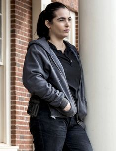 a woman leaning against a pillar in front of a brick building with her hands on her hips