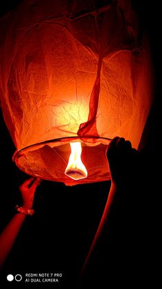 a person holding a lit up paper lantern in the dark with their hand on it