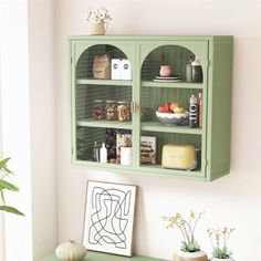 a green cabinet with glass doors on the wall above it and some plants in vases next to it