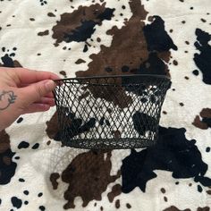 a hand holding a wire basket on top of a cow print rug with black and white spots