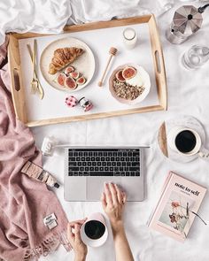 a person is using a laptop on a bed with breakfast and coffee in front of them