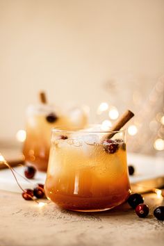 two glasses filled with drinks sitting on top of a table next to candles and berries