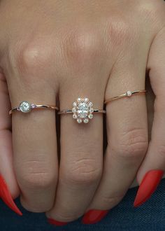 a woman's hand with red nails and two rings on her fingers, one ring has a flower