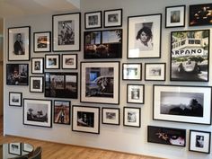 a wall filled with lots of framed pictures on top of a wooden floor next to a glass table