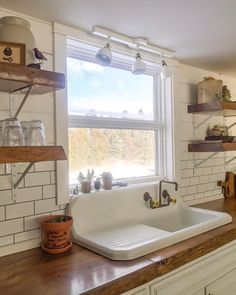 a white kitchen sink sitting under a window next to a wooden counter top with pots and pans on it