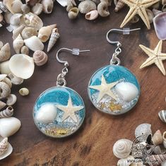 two starfishs and seashells in glass earrings on a wooden table surrounded by shells