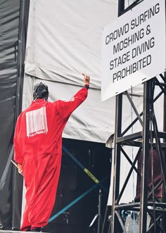 a man in a red suit standing on top of a stage next to a sign that says crowd surfing, moshing & stage diving prohibited