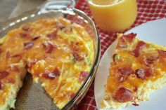 a slice of breakfast casserole on a plate next to a glass bowl with orange juice