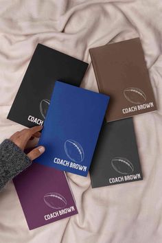 four coach brown notebooks laying on top of a white bed with the coach brown logo