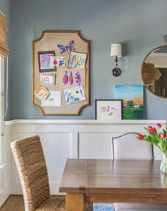 a dining room table and chairs with pictures on the wall above it, along with a vase filled with tulips