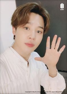 the young man is posing with his hand up in front of him and wearing a white shirt