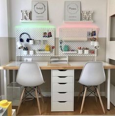 two white chairs sitting at a desk in front of a wall with shelves on it