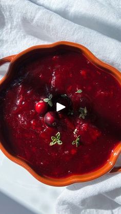 a red bowl filled with cranberry sauce on top of a white cloth