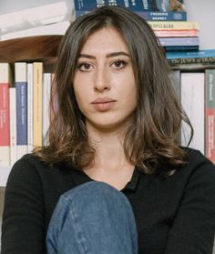 a woman sitting in front of a bookshelf with her legs crossed