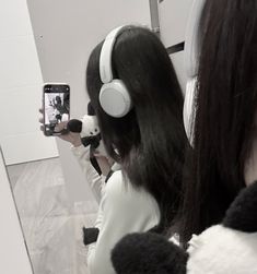 a woman taking a selfie in front of a mirror wearing headphones and holding a cell phone