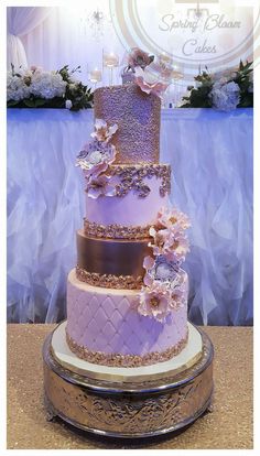 a three tiered wedding cake with purple flowers on the top and gold trimmings