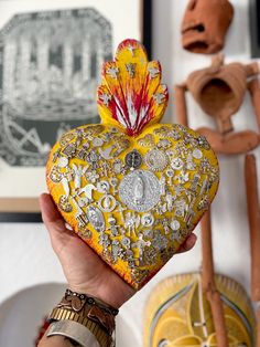 a person holding a decorative heart shaped object in front of some art on the wall