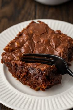 a piece of chocolate cake on a white plate with a fork stuck in the middle