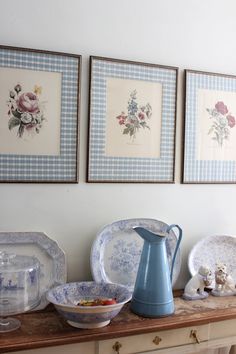 three framed pictures hang above a table with plates and bowls on it, along with a blue pitcher