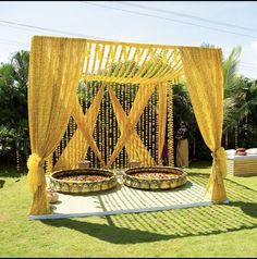 an outdoor ceremony setup with yellow drapes and flower baskets on the ground, surrounded by greenery