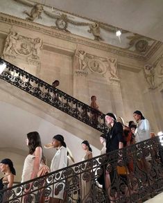 many people are walking up and down the stairs in an ornately decorated building with wrought iron railings