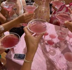 many people are holding up wine glasses with pink liquid in them and toasting at the same time