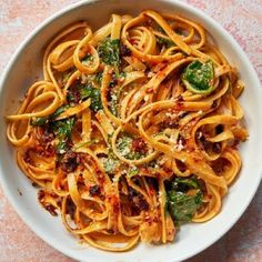 a white bowl filled with pasta and broccoli on top of a pink table