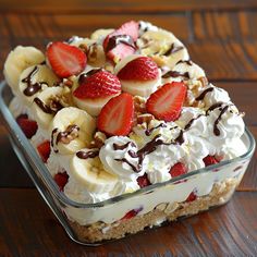 a dessert with bananas, strawberries and whipped cream in a glass dish on a wooden table