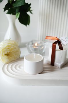 a white candle sitting on top of a table next to a vase